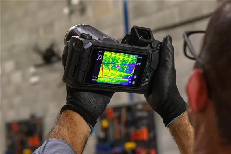 Técnico realiza inspeção elétrica com câmera térmica, destacando ponto quente em painel, prática essencial de segurança em termografia industrial.